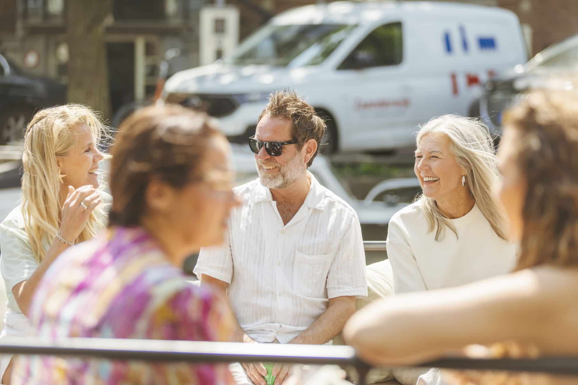 A group of people sitting together on a boat in Amsterdam, laughing and chatting while enjoying the cruise.