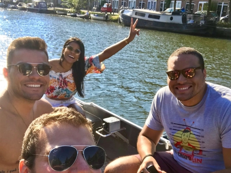 Three women and a man in white clothing on a boat, Boats4rent staff member on the quay