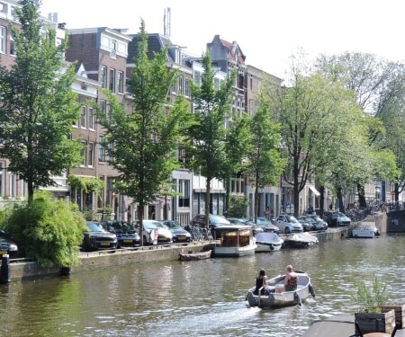 Two people sailing a boat on an Amsterdam canal.