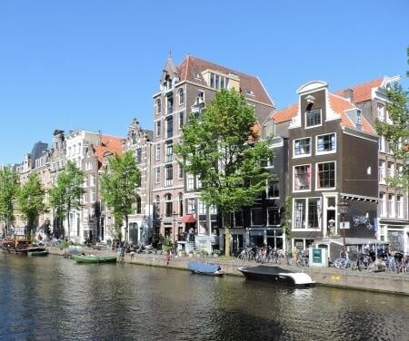 Canal houses along the Amsterdam canals with boats moored on a sunny day.